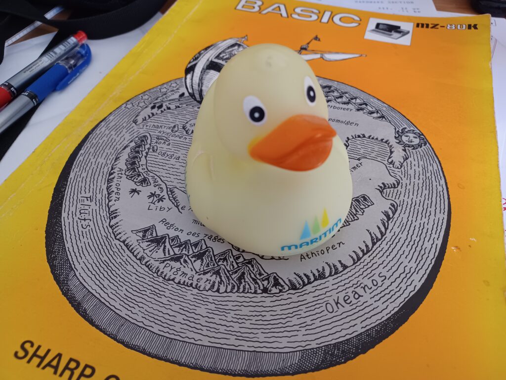 A yellow rubber duck on top of the Sharp MZ-80K BASIC manual. There are red and blue pens to one side.